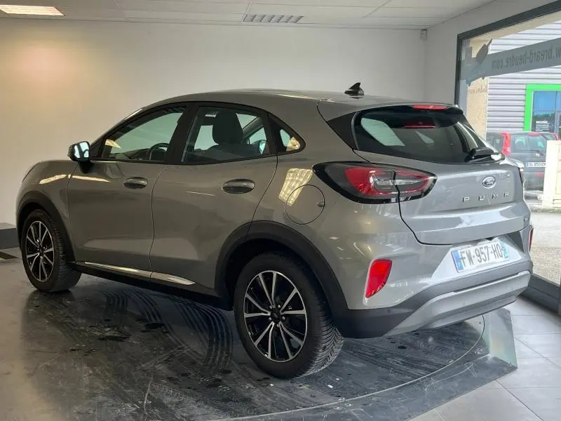 Ford Puma gris Solar métallisée vue 3/4 arrière droit avec jantes alu et feux arrière LED dans un showroom.