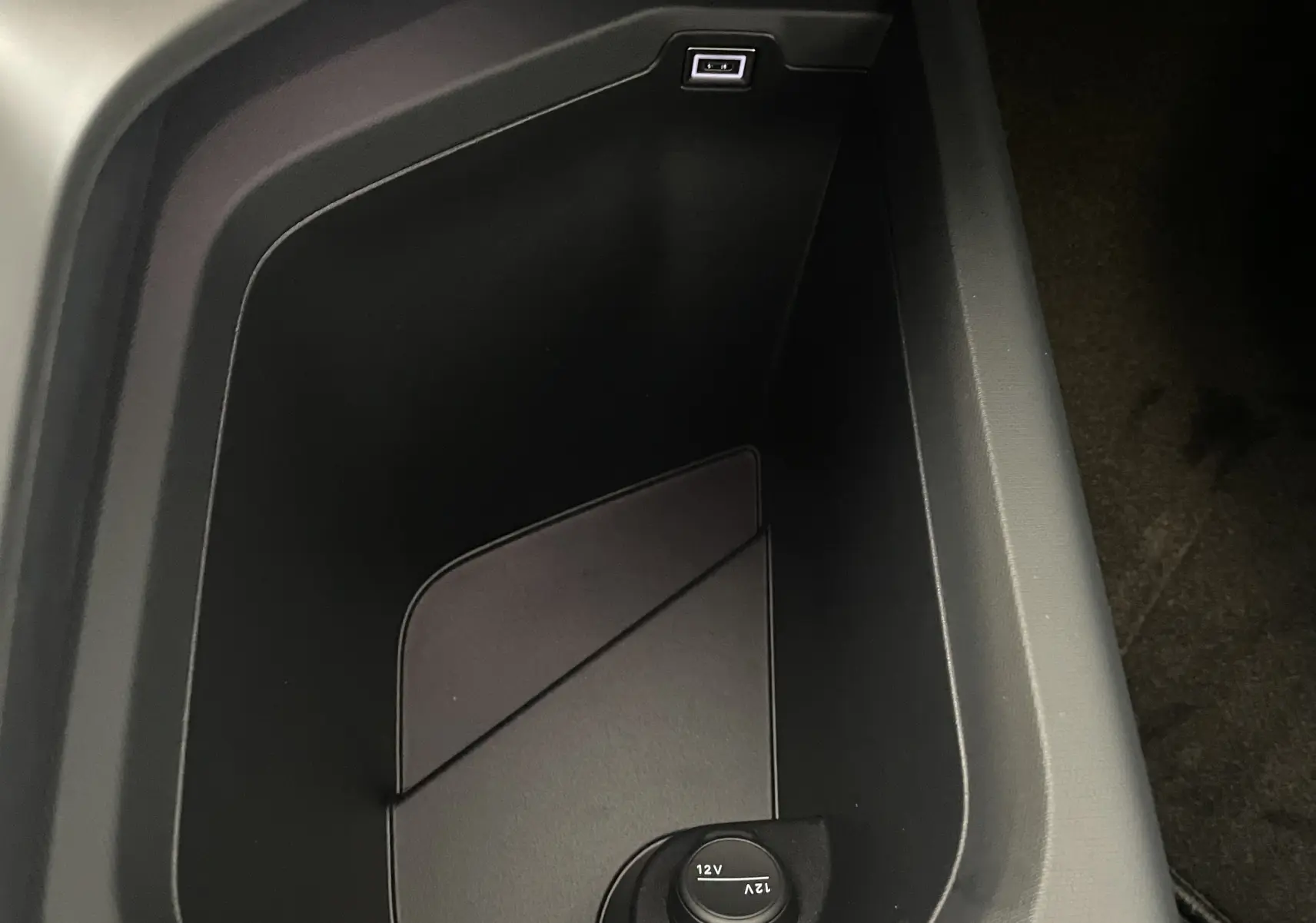 Vue rapprochée de la console centrale noire du Peugeot 3008 2025, montrant une prise USB et une prise 12V.