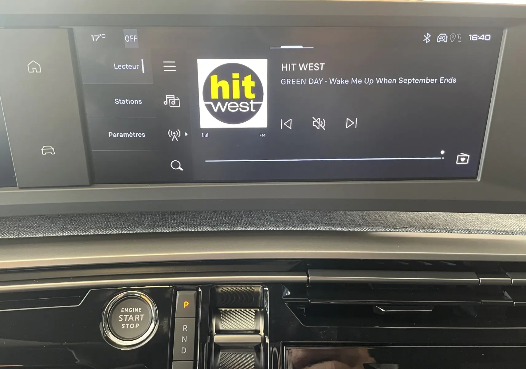 Écran tactile central et console noire du Peugeot 3008 Hybrid 2025 montrant la radio Hit West et bouton start/stop.