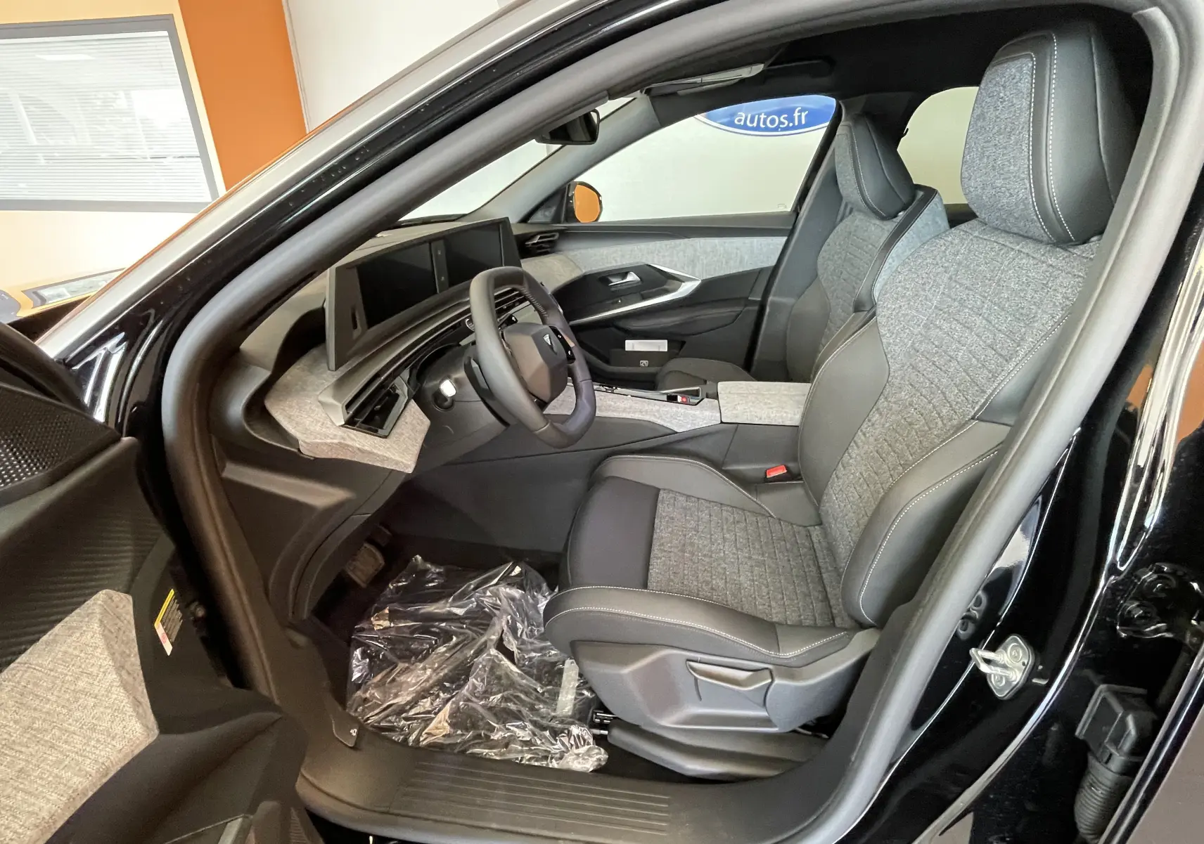 Intérieur côté conducteur du Peugeot 3008 noir 2025, sellerie tissu gris et tableau de bord avec double écran HD flottant.