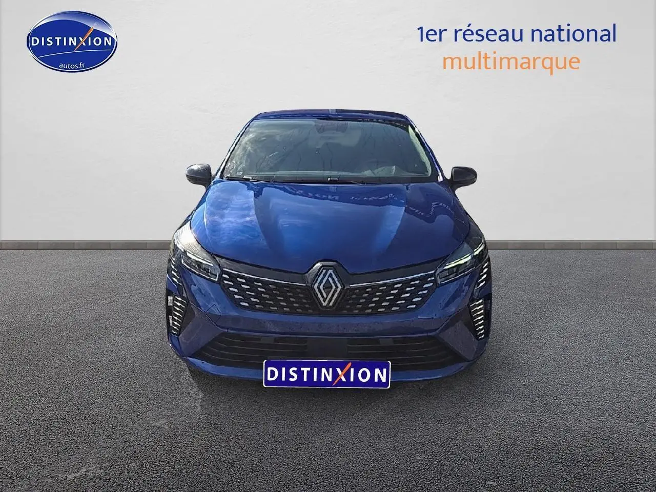 Vue frontale d'une Renault Clio V bleu iron avec calandre chromée et feux LED allumés sur fond neutre.