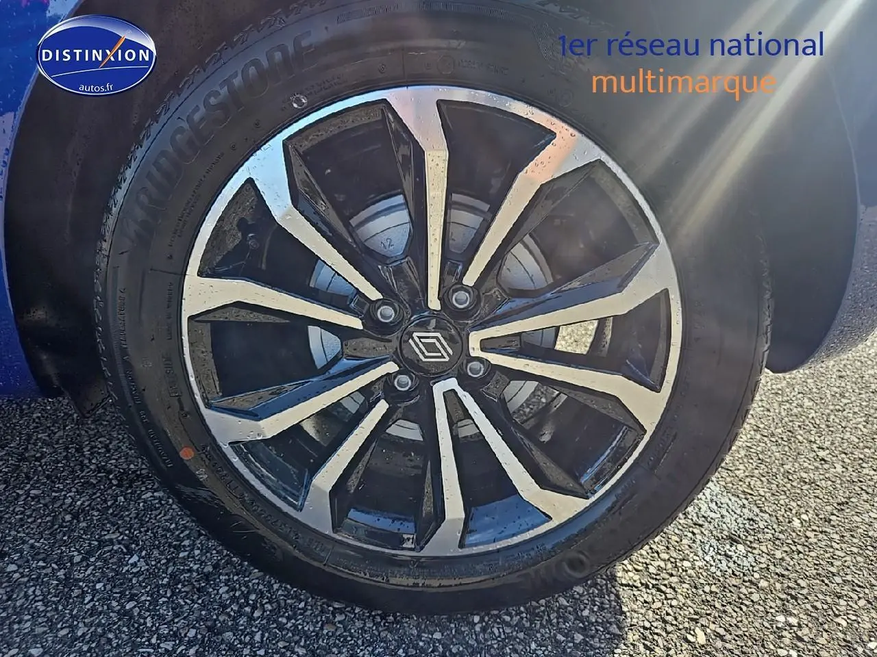 Gros plan sur la jante alu noire et argentée d'une Renault Clio V Bleu Iron, avec logo Renault au centre.