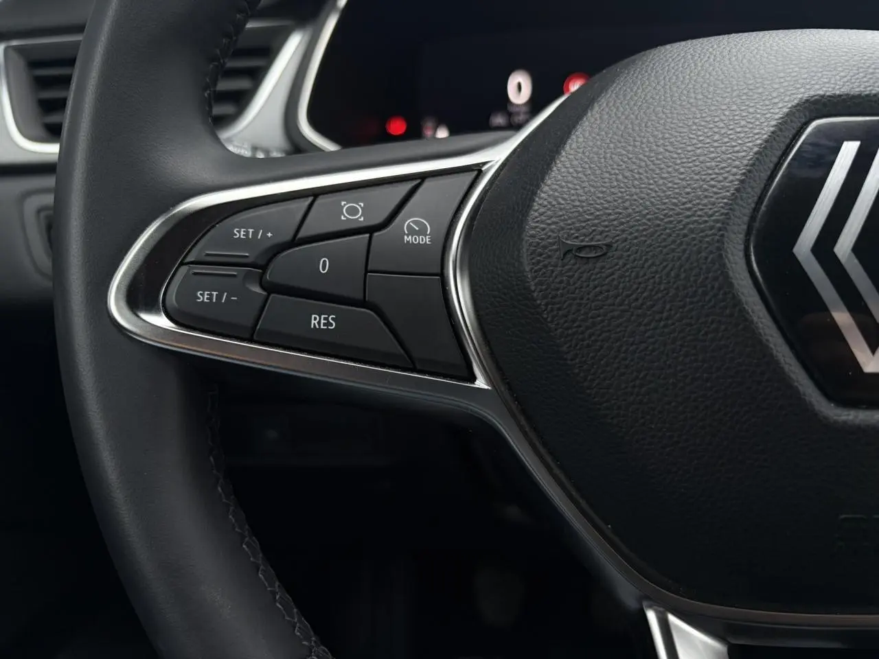 Gros plan sur la partie gauche du volant noir du Renault Captur 2025 avec commandes de régulateur et logo central.