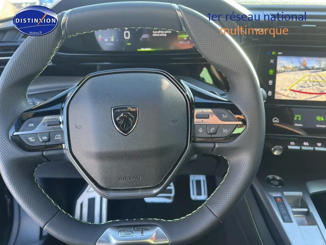 Vue rapprochée du volant cuir noir à surpiqûres vertes de la Peugeot 408 Hybrid 145 GT avec tableau de bord numérique et écran tactile.