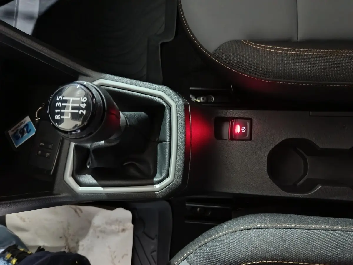 Vue rapprochée de la console centrale de la Dacia Sandero Extreme+ TCe 110 2024, avec levier de vitesse manuel et frein à main électrique allumé.