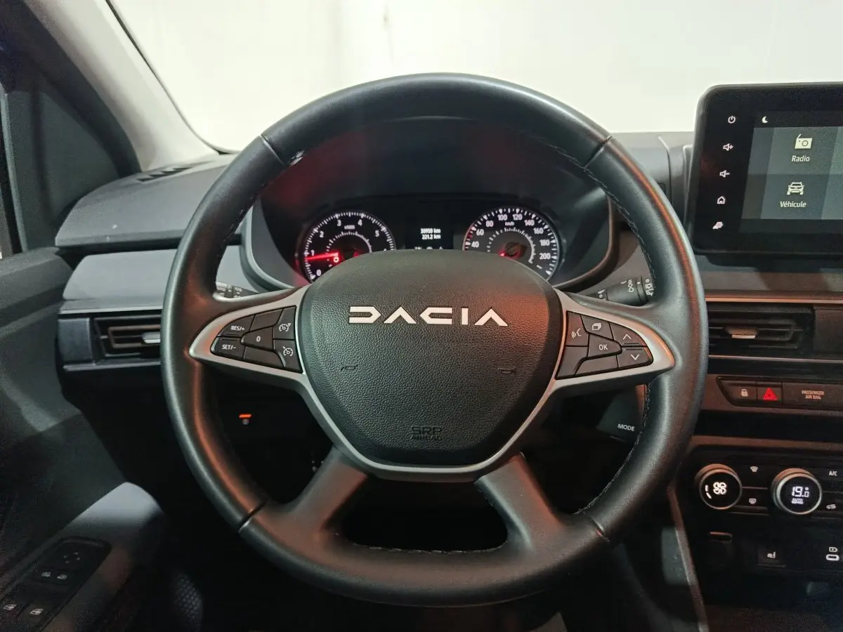 Vue rapprochée du volant cuir multifonctions noir du Dacia Sandero 2024 avec tableau de bord et écran tactile.