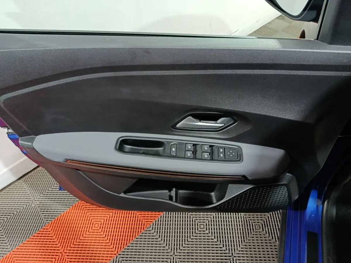 Vue intérieure côté gauche de la porte avant bleu de la Dacia Sandero Extreme+ avec commandes électriques des vitres et poignée grise.