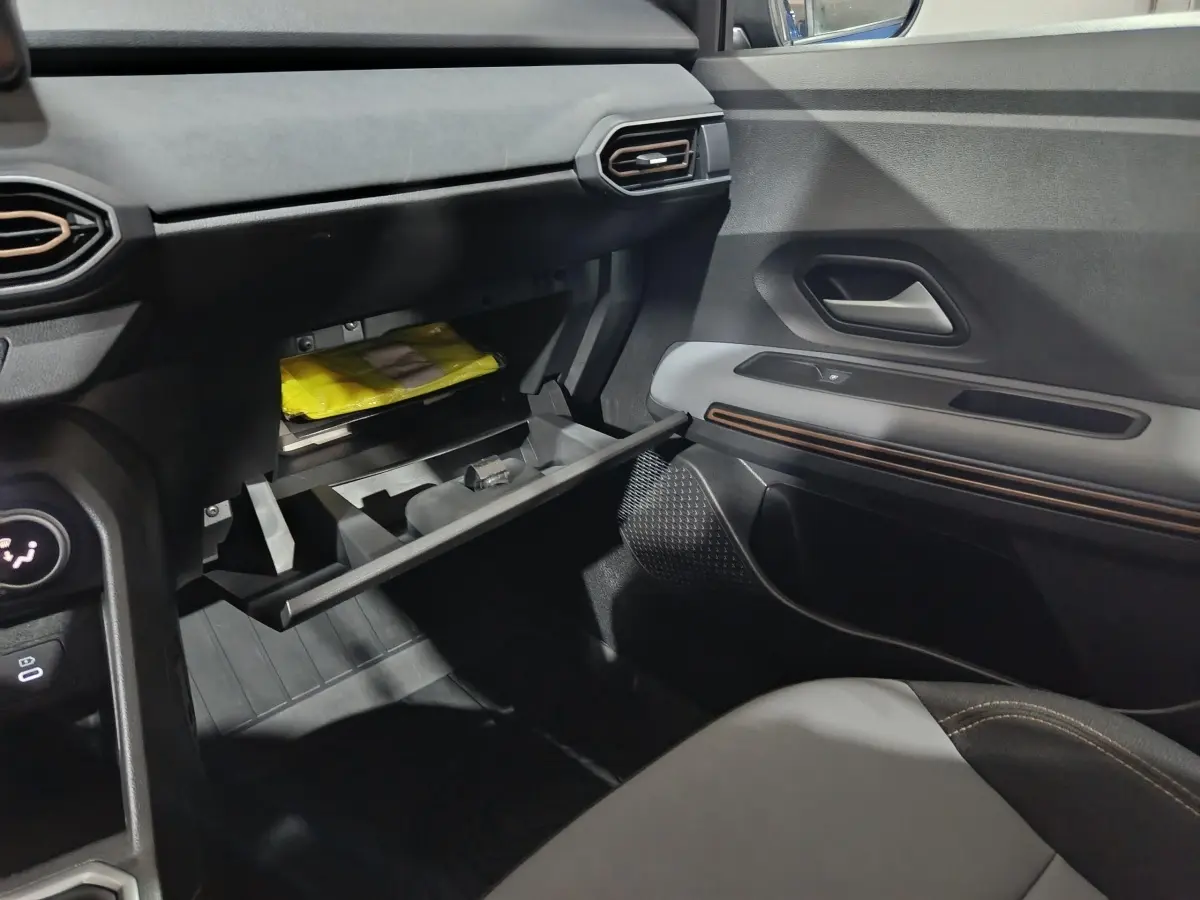 Intérieur de la Dacia Sandero Extreme+ 2024, vue côté passager sur la boîte à gants ouverte et la porte avec insert décoratif.