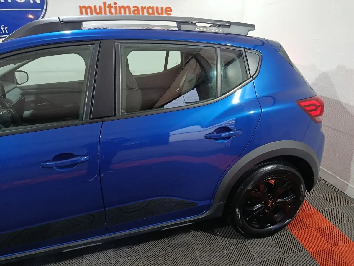 Vue côté droit arrière d'une Dacia Sandero Extreme+ TCe 110 2024 bleu avec jantes noires et logo Stepway sur le montant arrière.