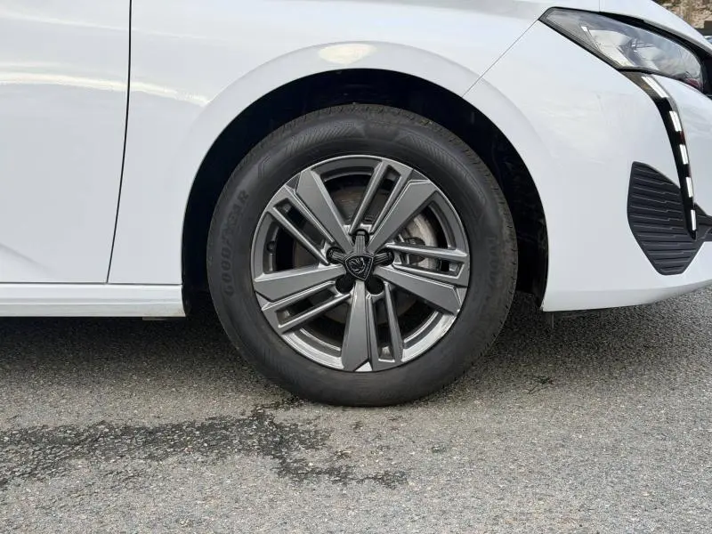 Gros plan sur la roue avant droite de la Peugeot 308 2024 blanche Okénite, avec jante alliage et partie avant du pare-chocs visible.