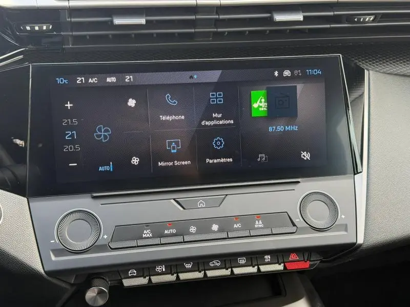 Écran tactile central et commandes climatisation du tableau de bord de la Peugeot 308 2024 blanc Okénite, vue intérieure frontale.
