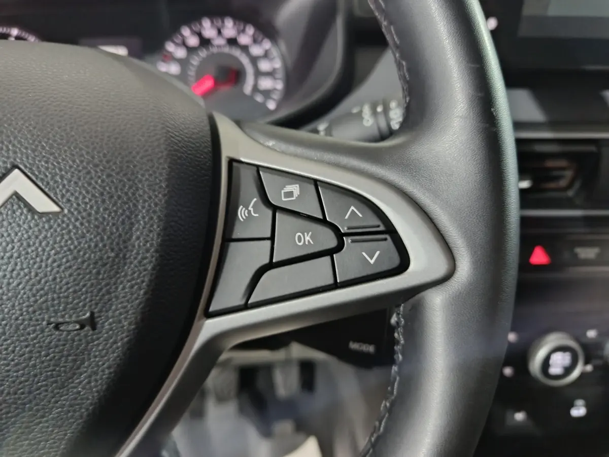 Gros plan sur le volant cuir noir de la Dacia Sandero 2024 avec commandes multifonctions et tableau de bord flou.