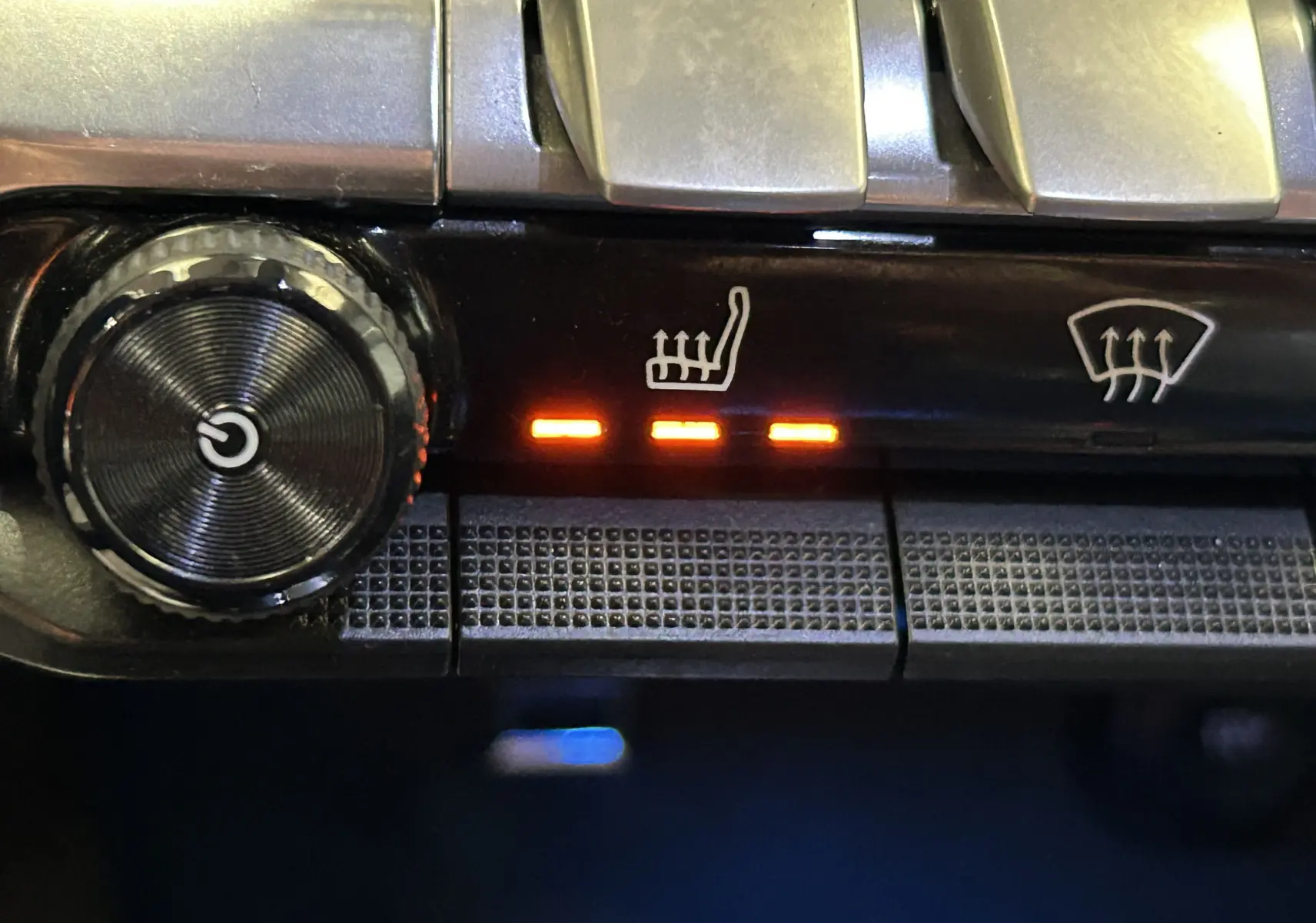 Gros plan sur les commandes de chauffage des sièges du Peugeot 5008 gris, avec trois voyants orange allumés.