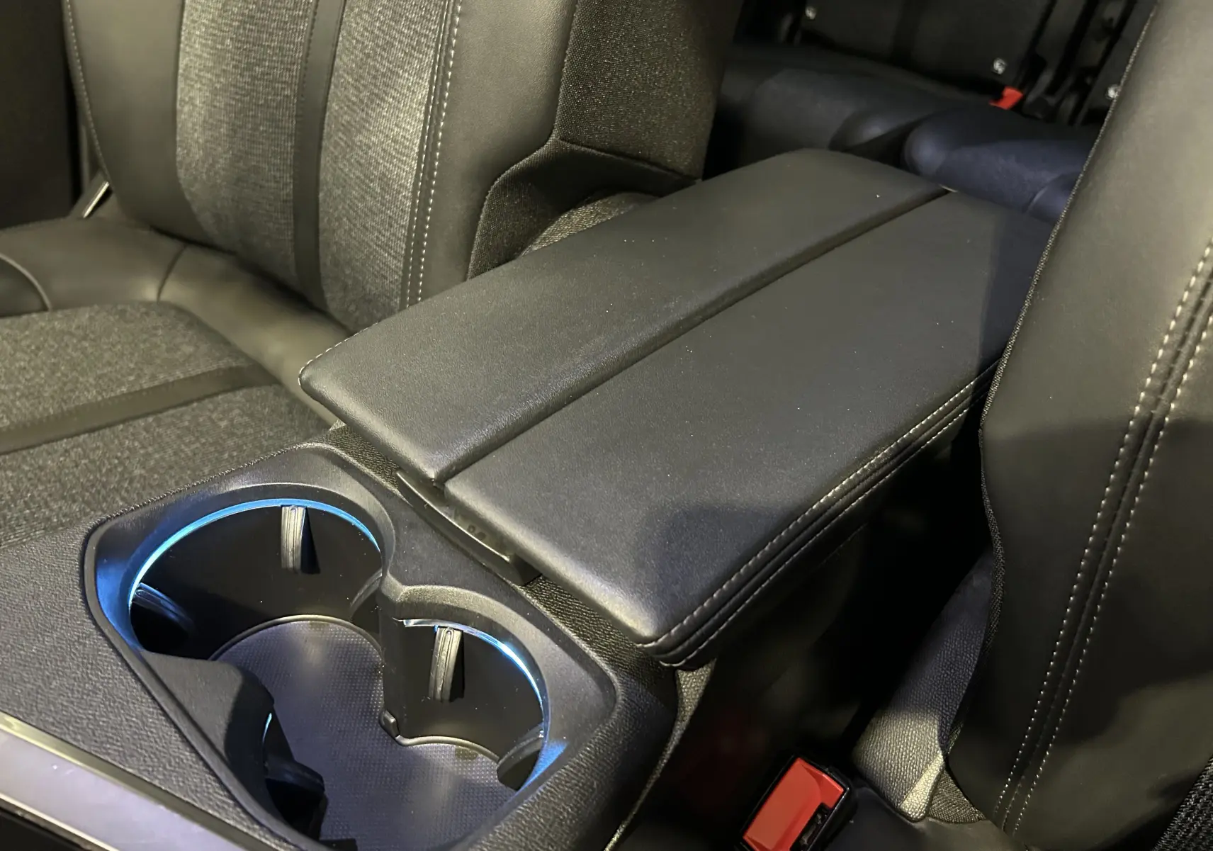 Gros plan sur l'accoudoir central noir et porte-gobelets éclairés à l'intérieur du Peugeot 5008 gris 2020.