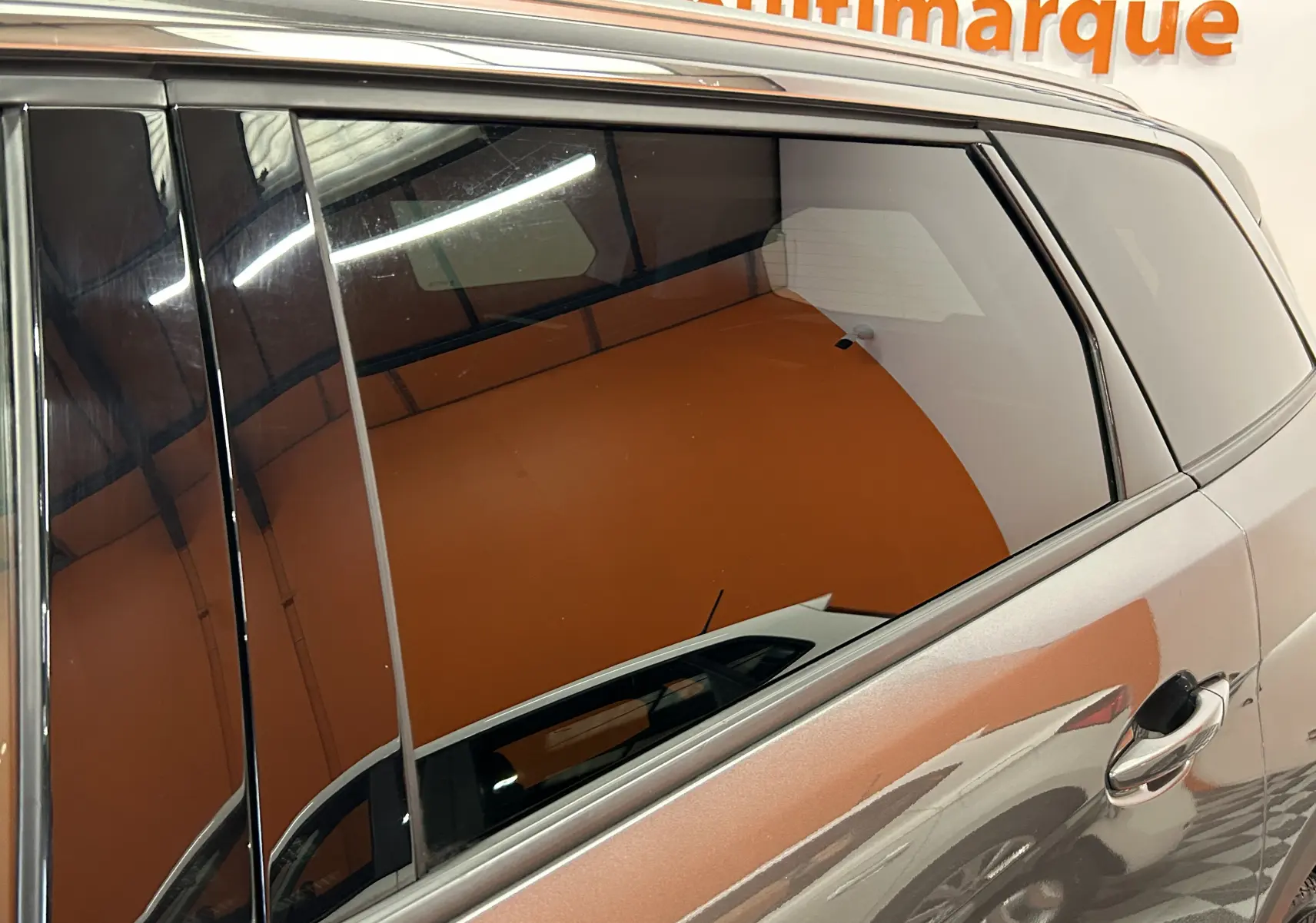 Vue latérale côté droit du Peugeot 5008 gris métallisé avec vitres teintées en intérieur showroom.