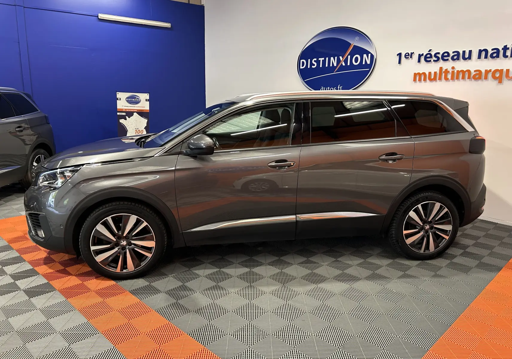 Peugeot 5008 gris métallisé vue de profil côté gauche, avec jantes alliage et vitres teintées dans un showroom.