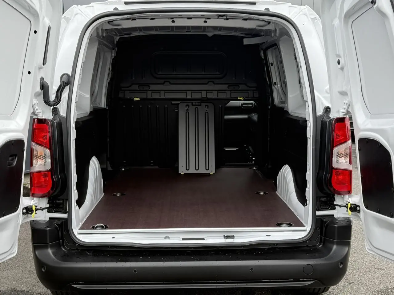Vue arrière ouverte du Peugeot Partner blanc 2025, montrant l'espace de chargement avec plancher bois antidérapant et anneaux d'arrimage.