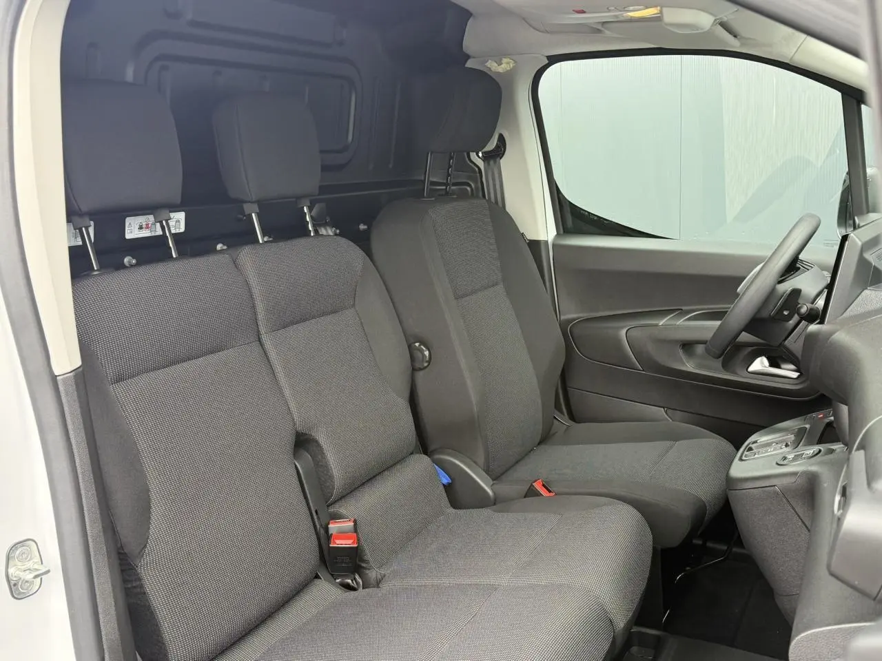 Vue intérieure côté conducteur du Peugeot Partner XL 2025 blanc, montrant la banquette 3 places en tissu gris foncé.