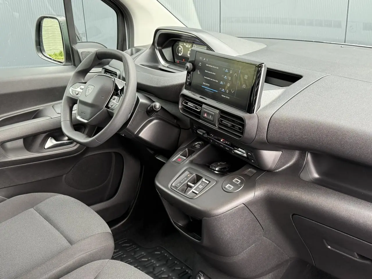 Vue intérieure côté conducteur du Peugeot Partner 2025, tableau de bord noir avec écran tactile et volant multifonctions.