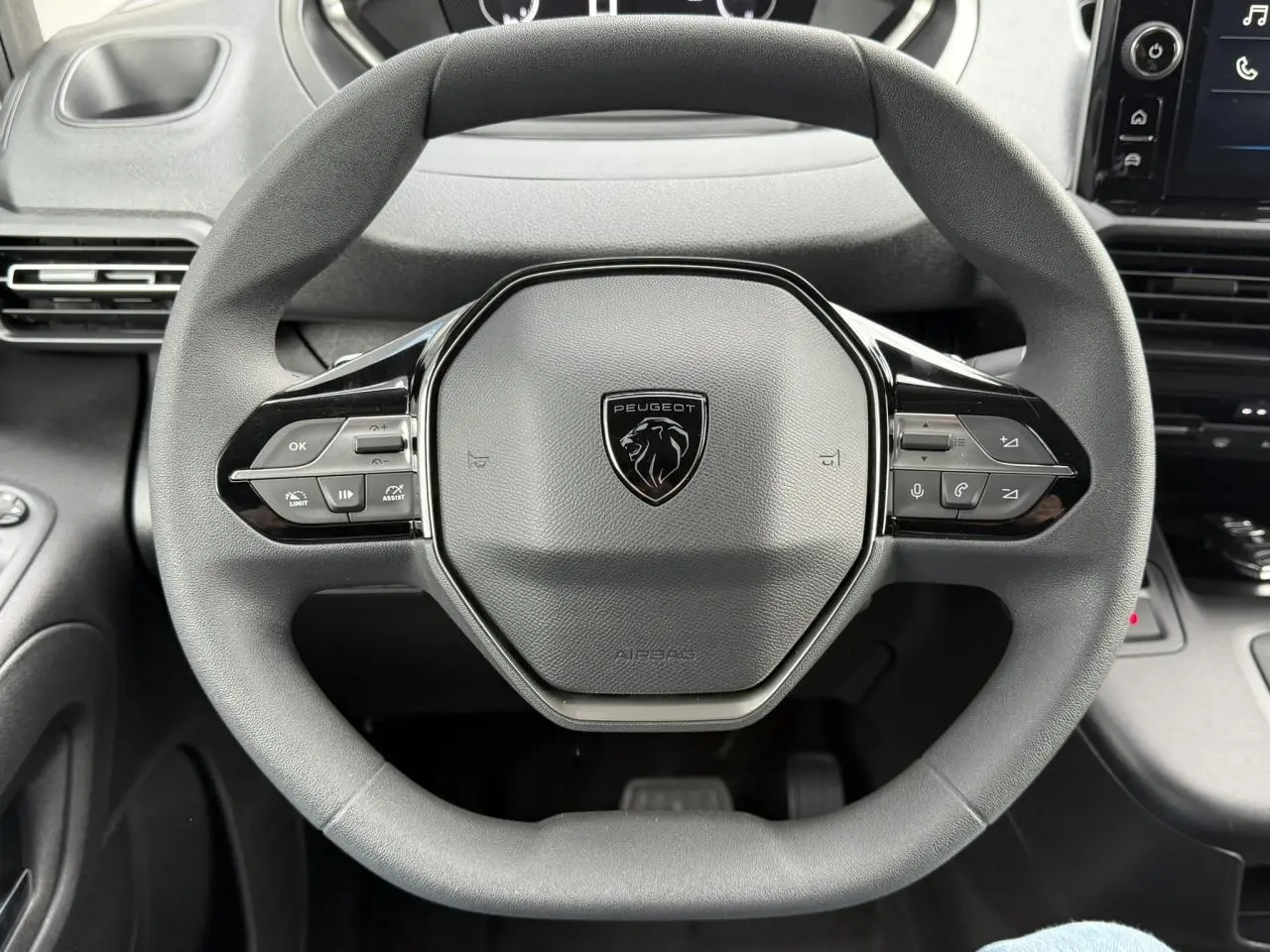 Vue rapprochée du volant multifonctions noir du Peugeot Partner 2025 avec logo lion au centre et commandes intégrées.