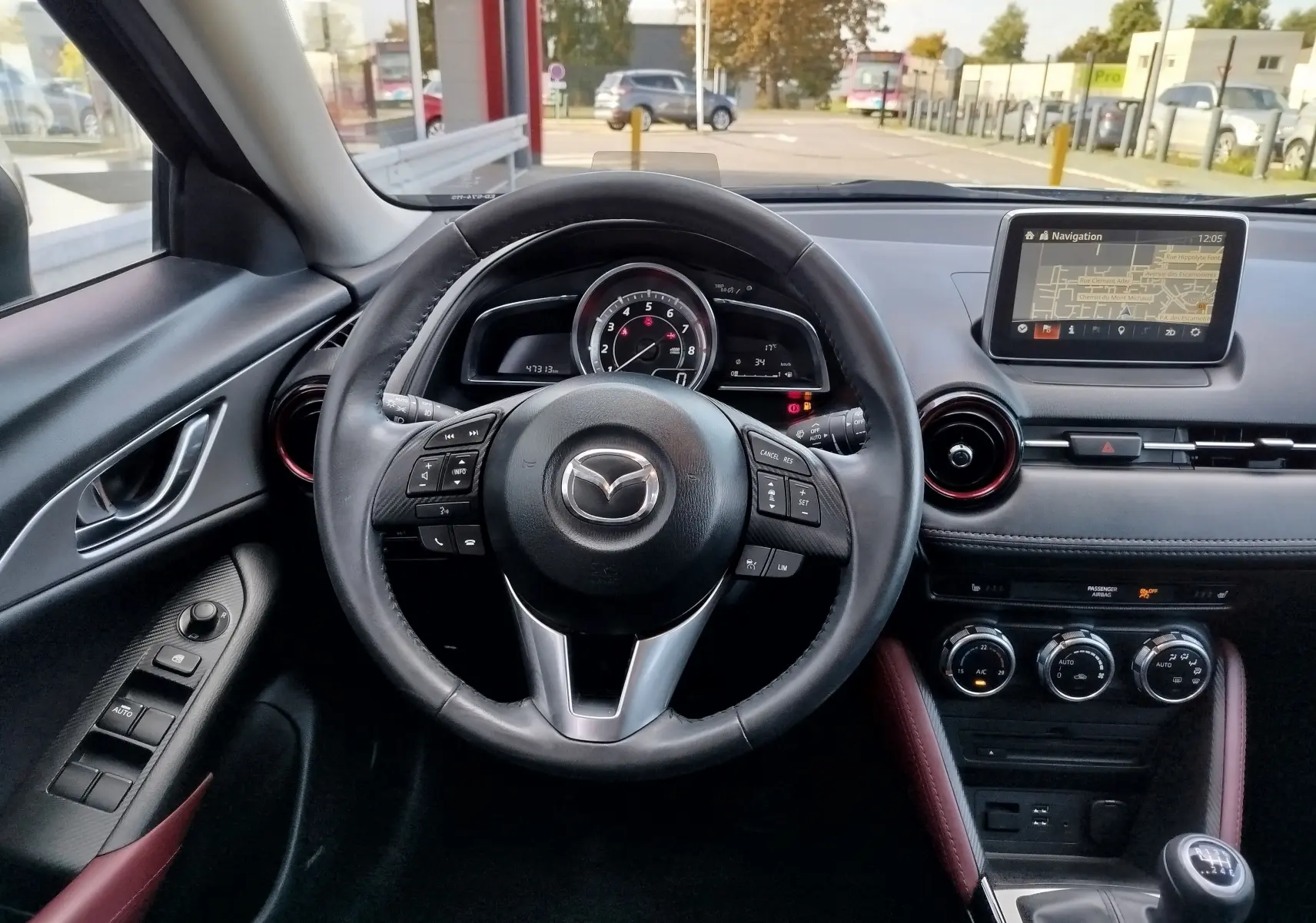 Vue intérieure frontale du tableau de bord du Mazda CX-3 bleu, avec volant cuir, écran navigation et boîte manuelle.