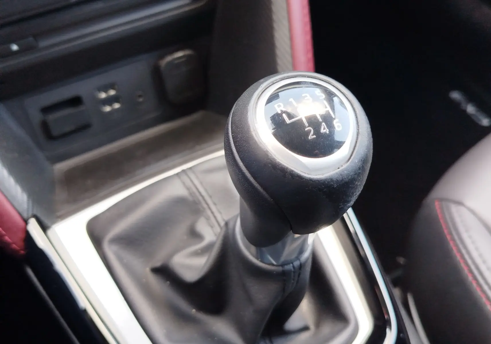 Gros plan sur le levier de vitesses manuel noir du Mazda CX-3 2016, avec coutures rouges visibles sur le siège adjacent.