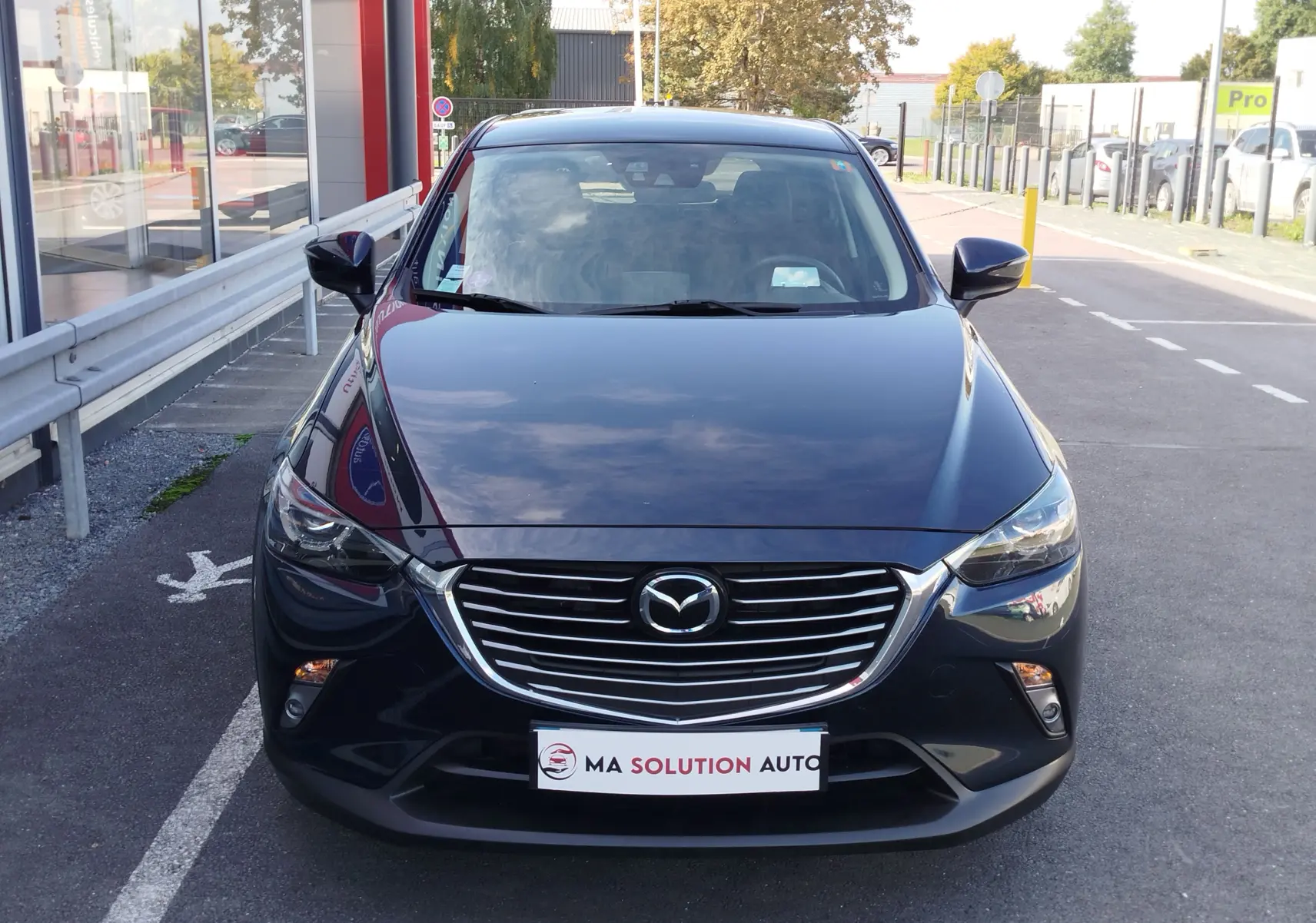 Vue frontale d'un Mazda CX-3 2016 bleu foncé avec calandre chromée et phares LED allumés.