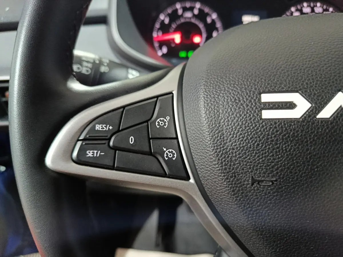 Gros plan sur le volant multifonctions en cuir synthétique noir de la Dacia Sandero Extreme+ bleu, avec commandes de régulateur.