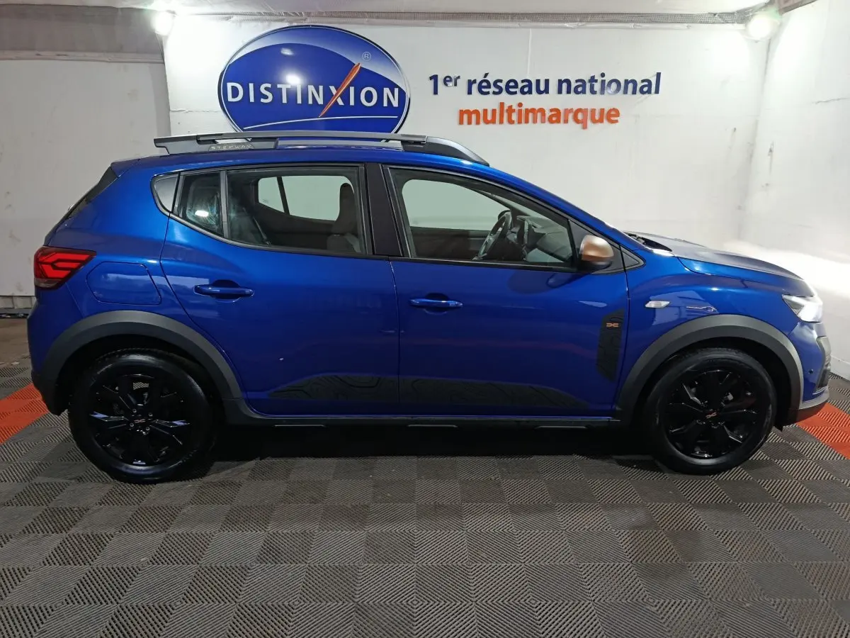 Profil droit d'une Dacia Sandero Extreme+ TCe 110 2024 bleu avec jantes noires et rails de toit assortis.