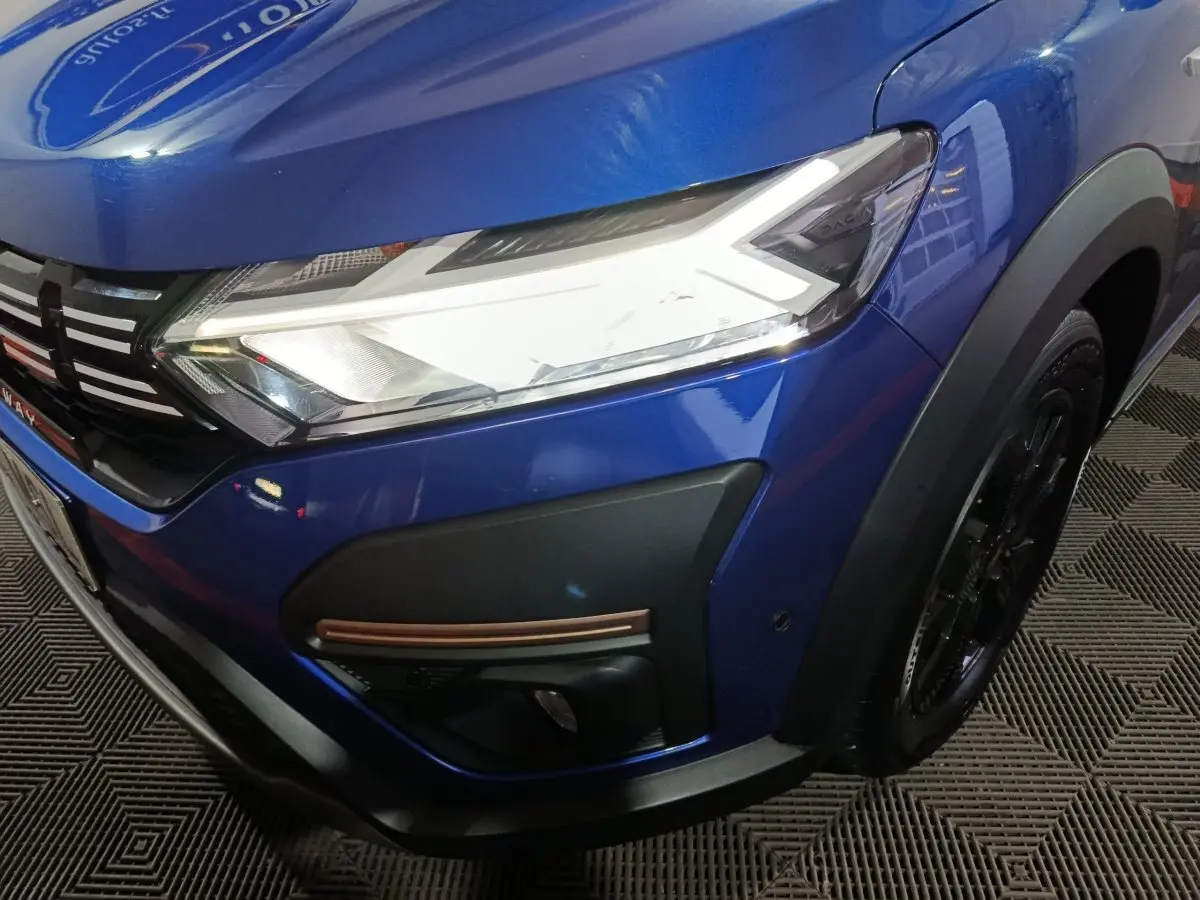 Gros plan sur l'avant droit bleu de la Dacia Sandero Extreme+ 2024 avec phares LED et détails noirs et cuivrés.