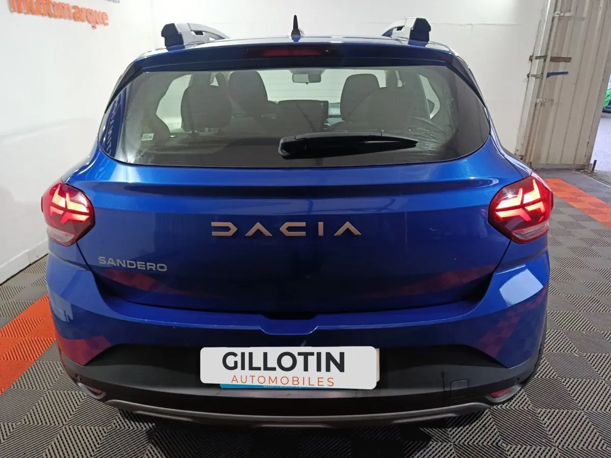 Vue arrière d'une Dacia Sandero Extreme+ TCe 110 bleu 2024 avec feux LED allumés et toit équipé de rails assortis.