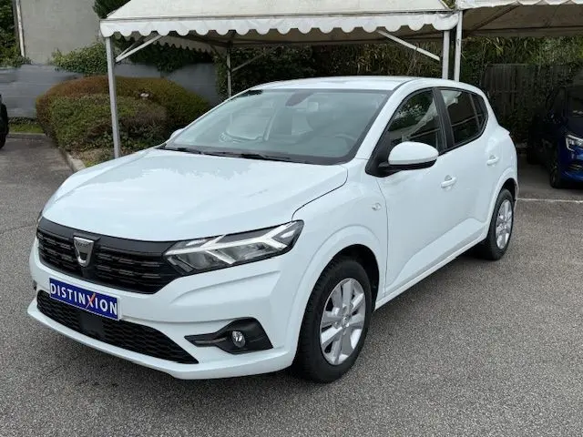Dacia Sandero 2023 blanc glacier vue 3/4 avant droit, calandre noire et jantes alliage argentées visibles.