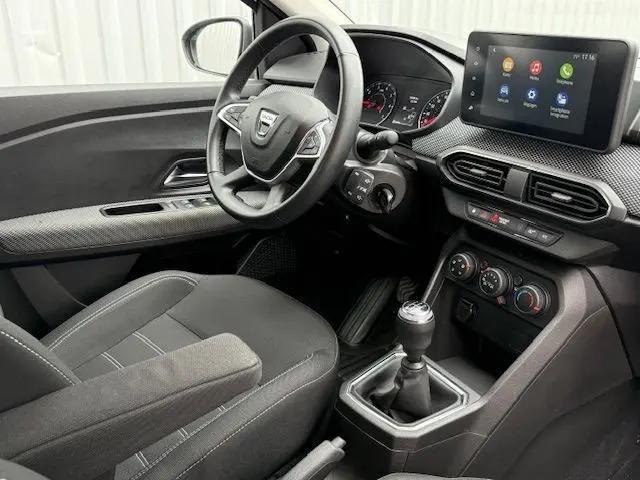 Vue intérieure côté conducteur de la Dacia Sandero 2023, volant multifonction et écran tactile central visibles.