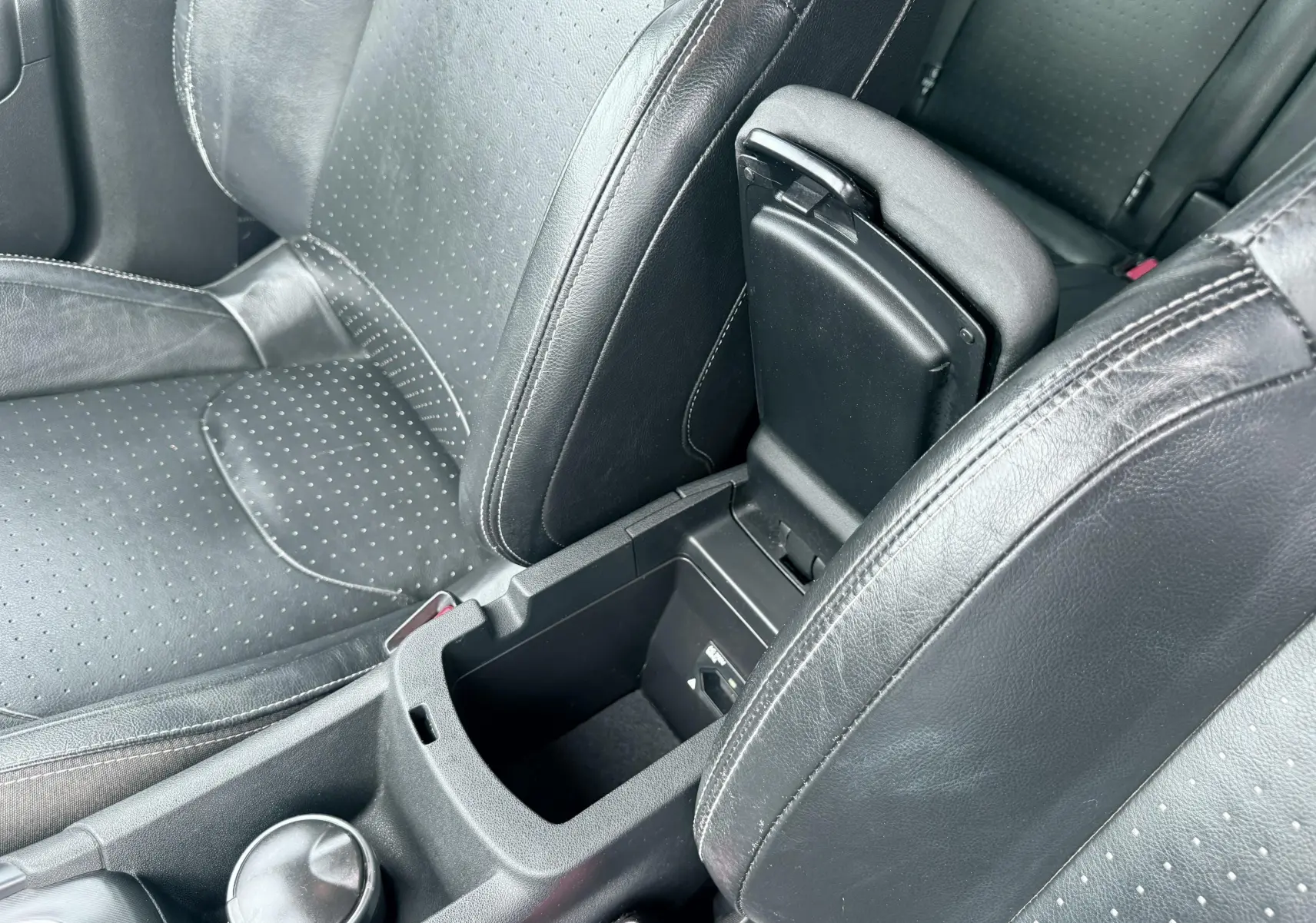 Vue rapprochée de l’intérieur noir en cuir perforé du Citroën DS4, avec accoudoir central ouvert et console visible.