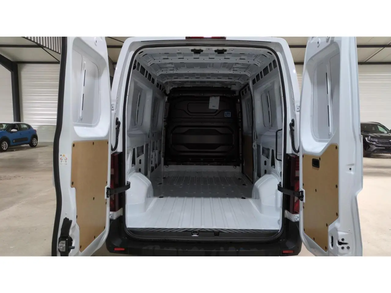 Vue arrière du Renault Master blanc 2025 avec portes ouvertes montrant l'espace de chargement vide et les panneaux intérieurs en bois.