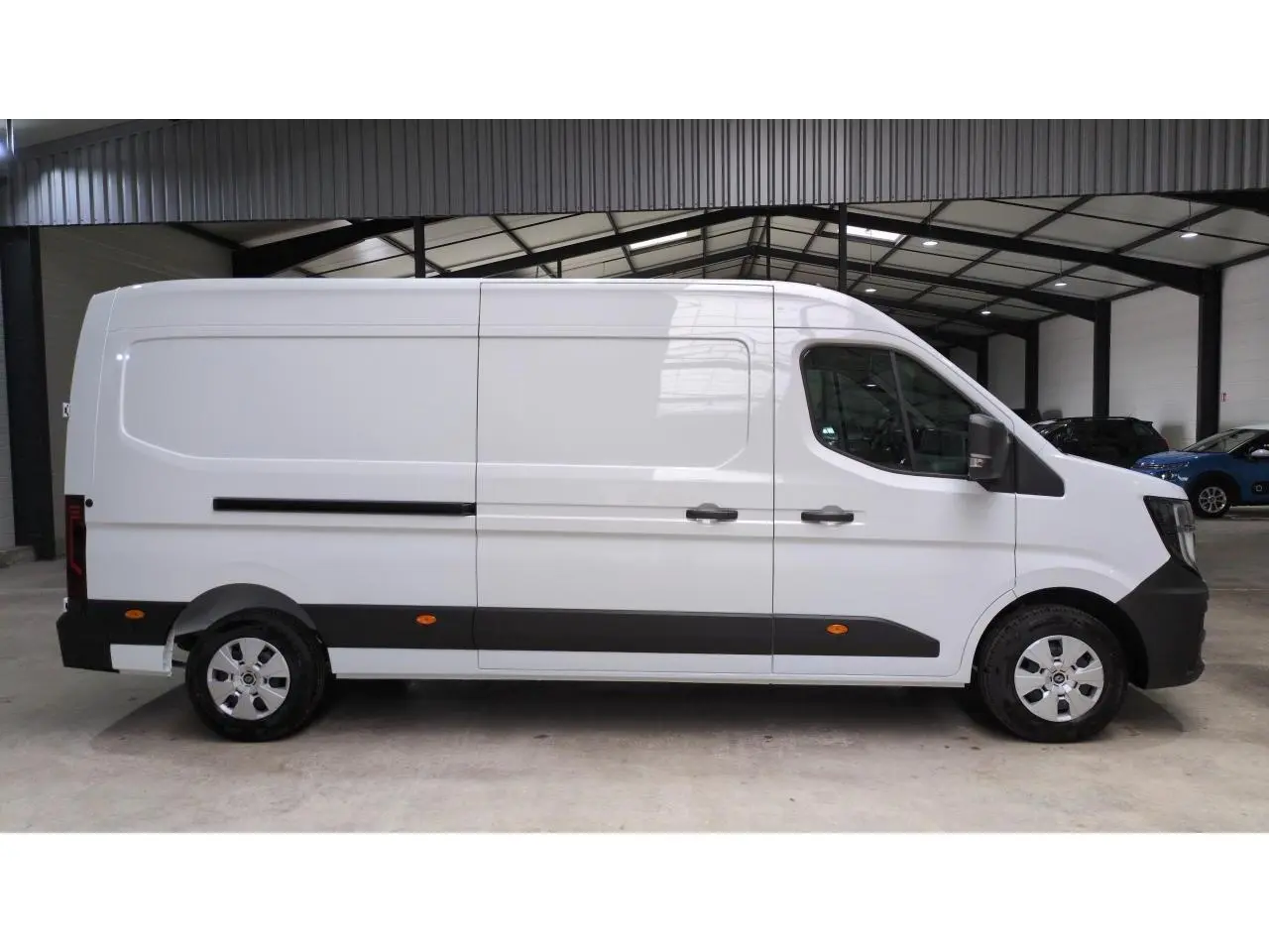 Profil côté droit du Renault Master blanc 2025 avec bandeau noir et roues argentées dans un garage.