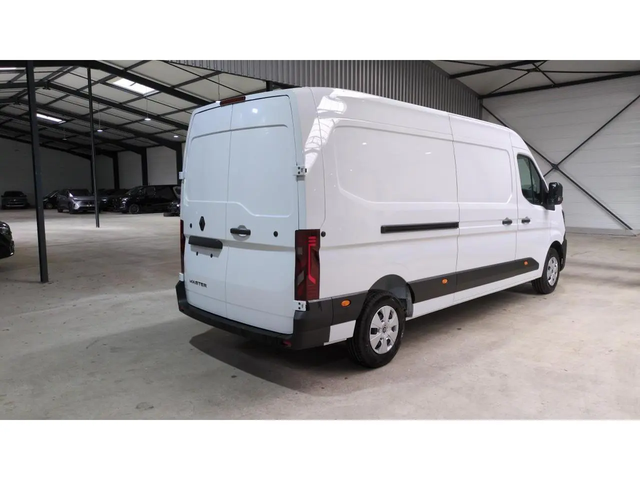 Renault Master blanc vu en 3/4 arrière droit dans un grand garage, avec feux arrière verticaux et protections noires.
