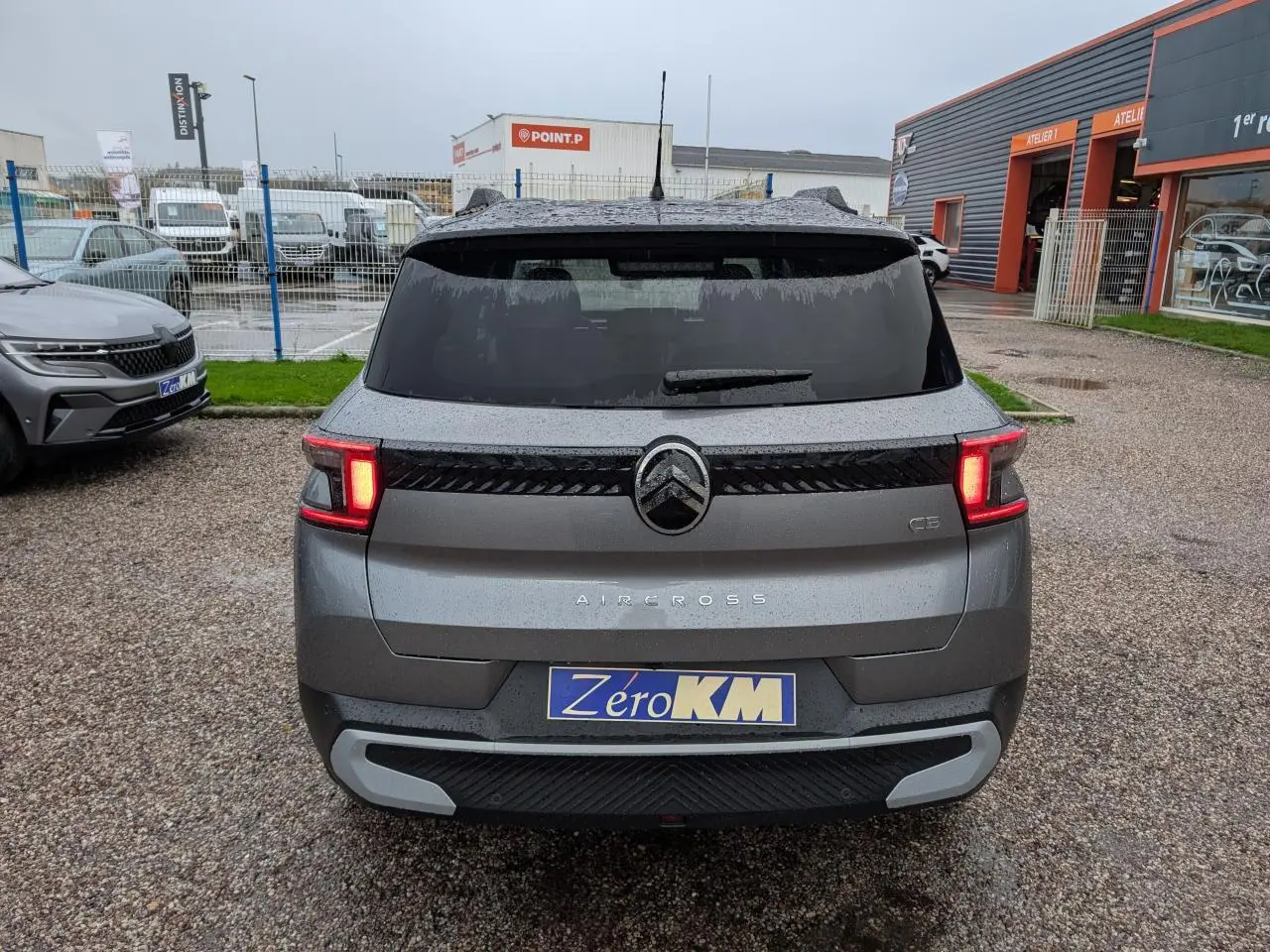 Vue arrière du Citroën C3 Aircross gris métallisé avec toit noir et feux arrière LED allumés sur parking humide.