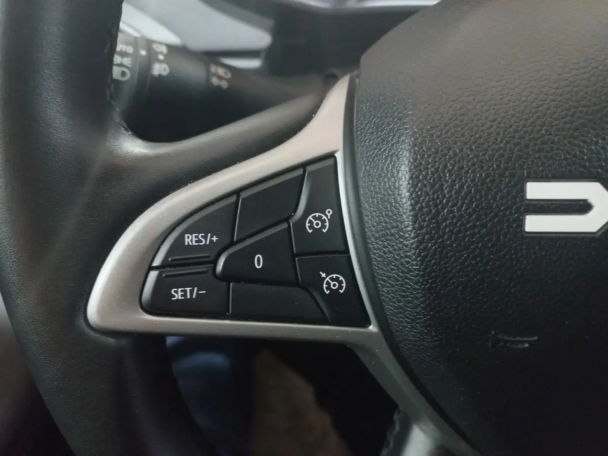 Gros plan sur les commandes de régulateur de vitesse au volant en cuir synthétique noir de la Dacia Sandero 2024.