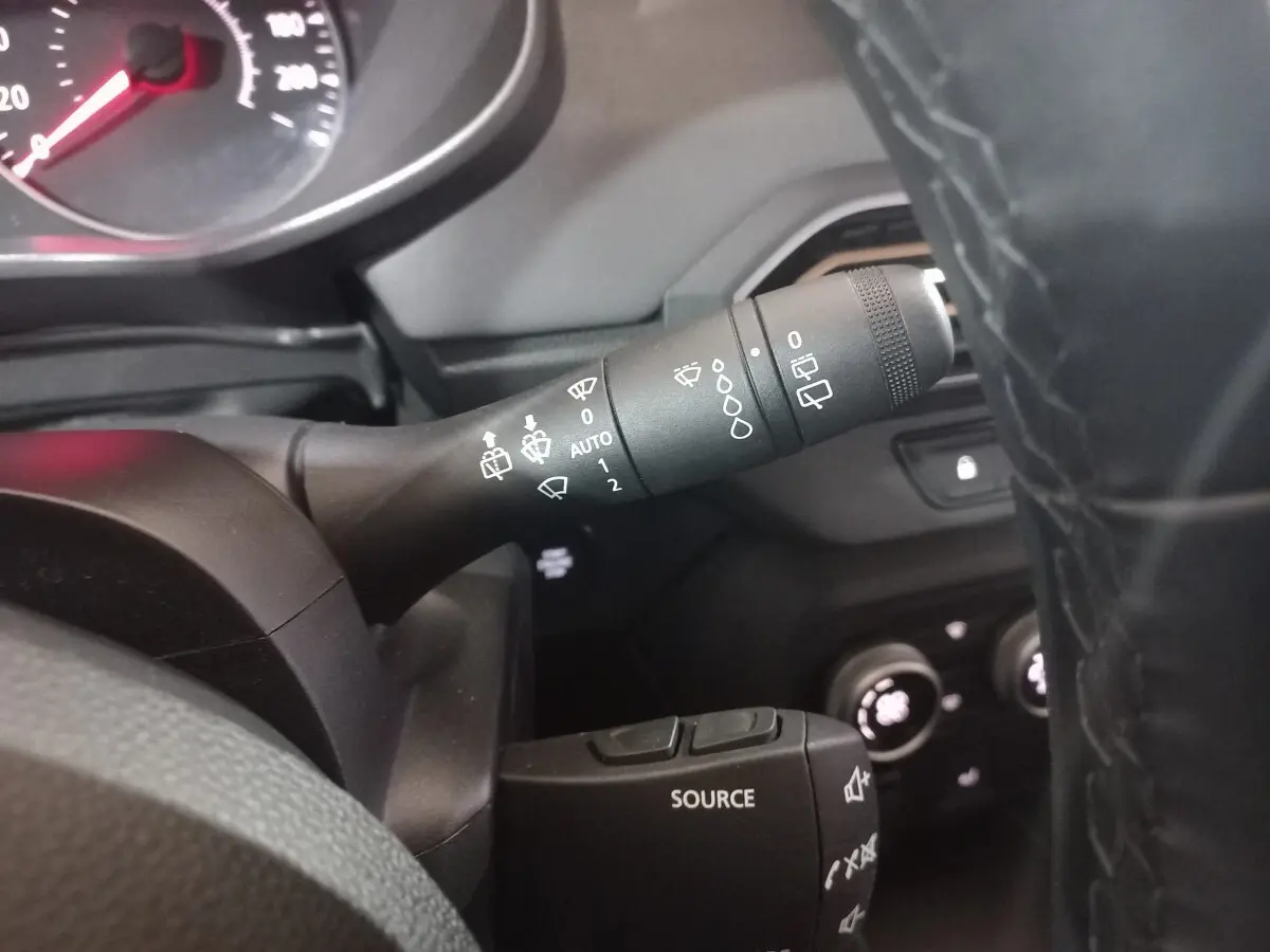 Gros plan sur la commande des essuie-glaces à gauche du volant cuir noir dans le tableau de bord d’une Dacia Sandero verte 2024.