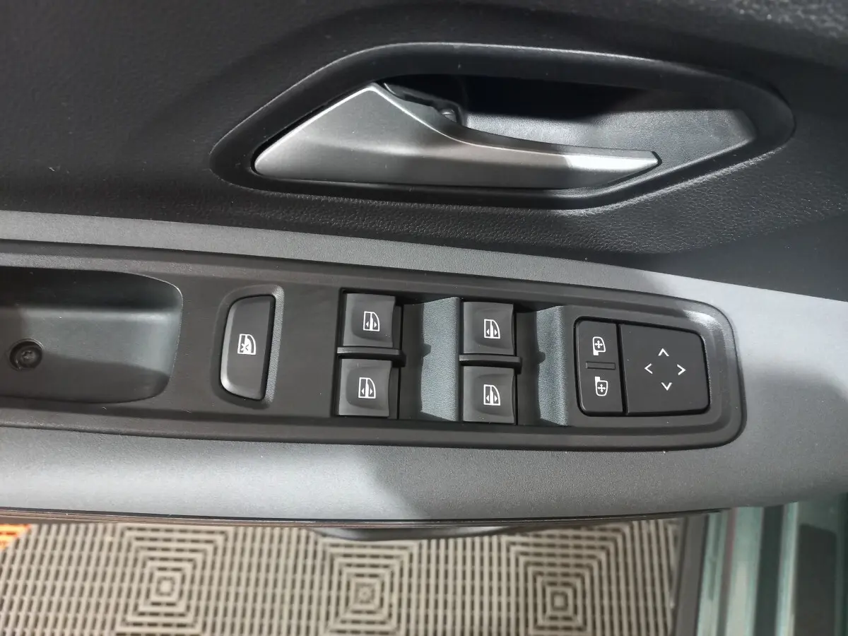 Vue rapprochée des commandes de lève-vitres et rétroviseurs sur la portière côté conducteur d'une Dacia Sandero 2024 vert.