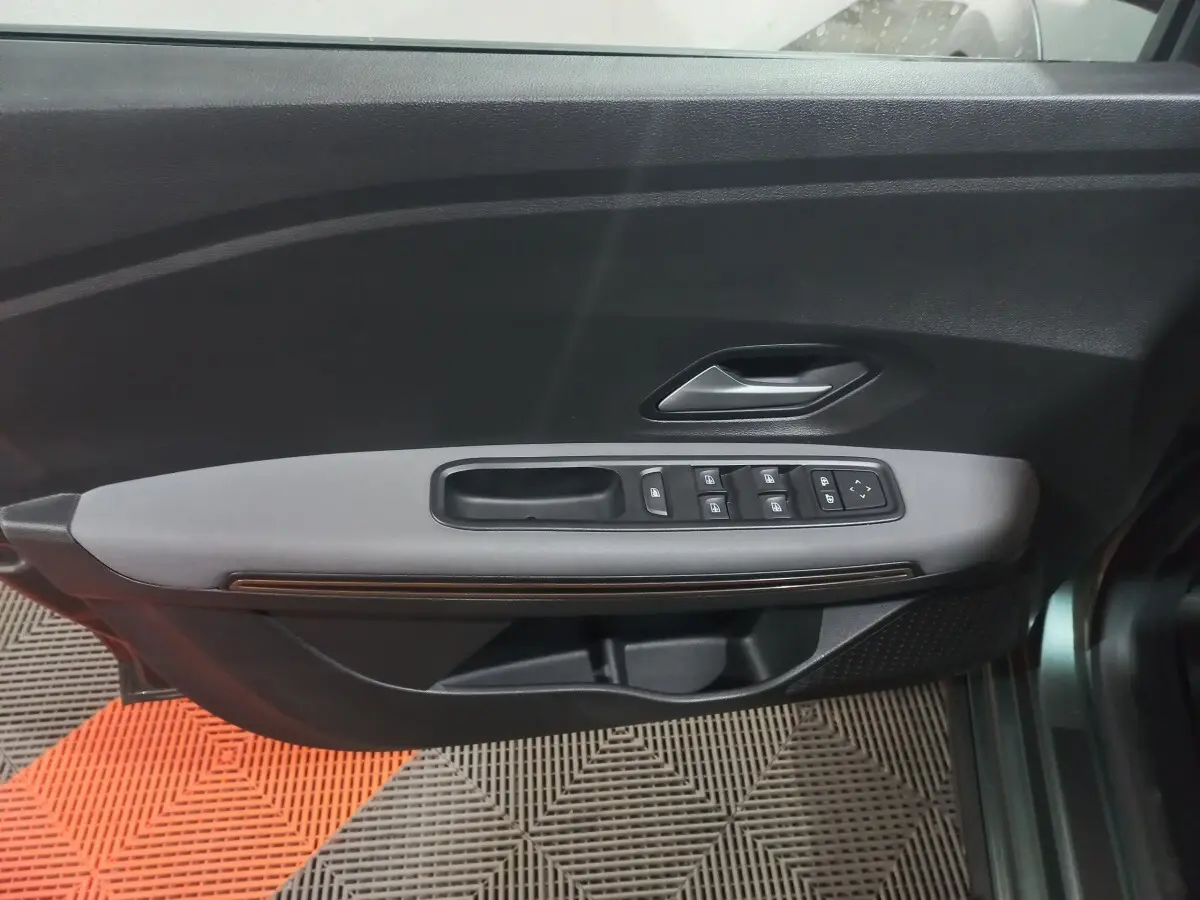 Vue rapprochée de la porte avant gauche verte de la Dacia Sandero 2024 avec commandes électriques des vitres et poignée intérieure.
