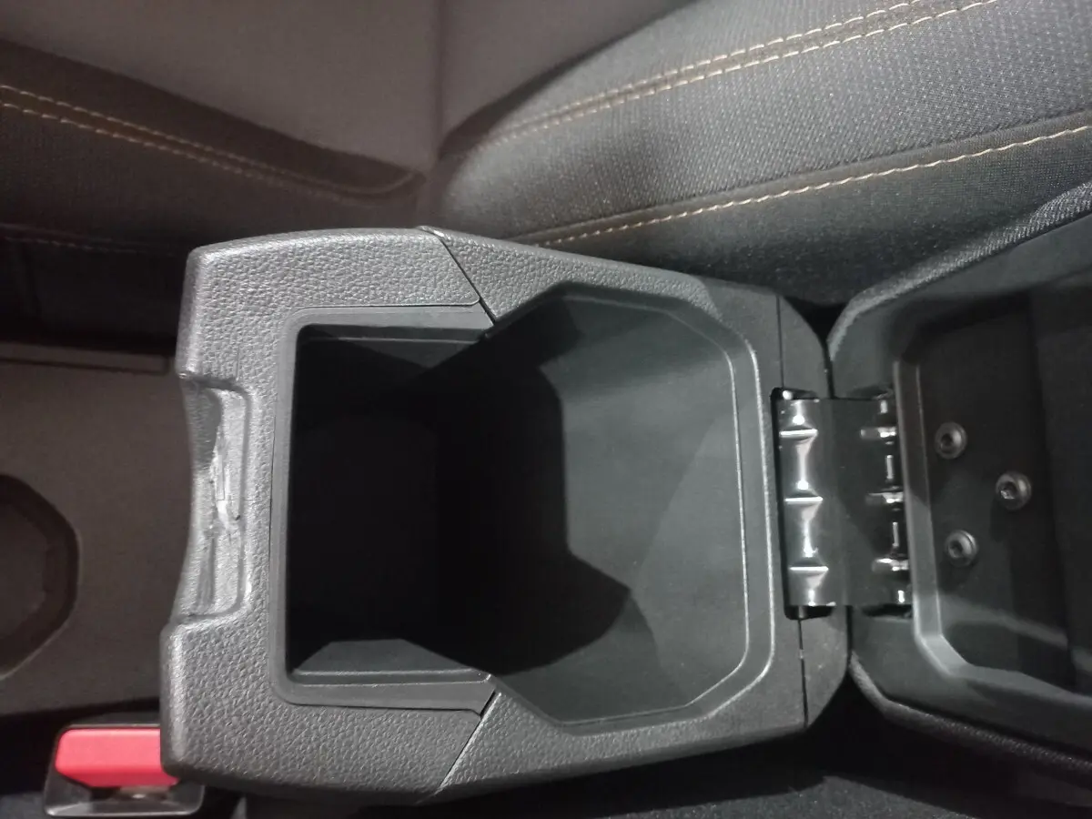 Gros plan sur le rangement central ouvert entre les sièges avant du Dacia Sandero 2024, tissu gris avec surpiqûres beiges.