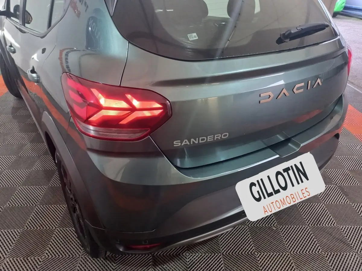 Vue 3/4 arrière droite d'une Dacia Sandero verte avec feux arrière allumés et logo visible sur le hayon.