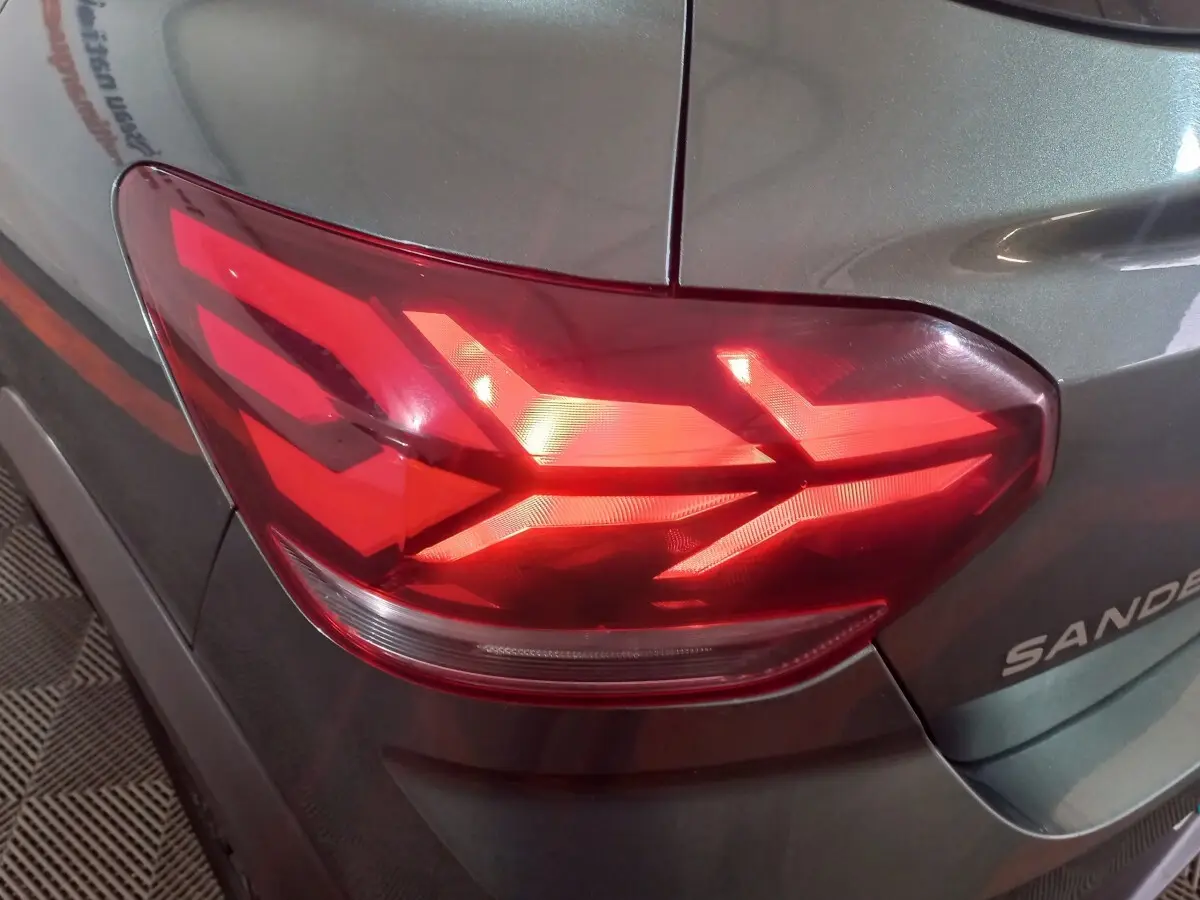 Gros plan sur le feu arrière droit rouge d'une Dacia Sandero 2024 vert foncé, avec logo partiel visible sur la malle.