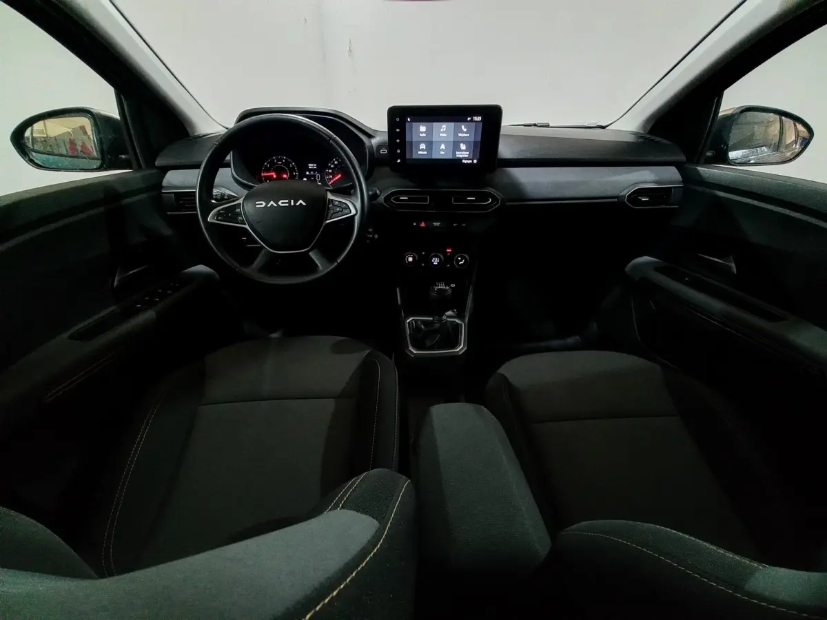 Vue intérieure avant de la Dacia Sandero 2024, tableau de bord avec écran tactile central et volant multifonctions noir.