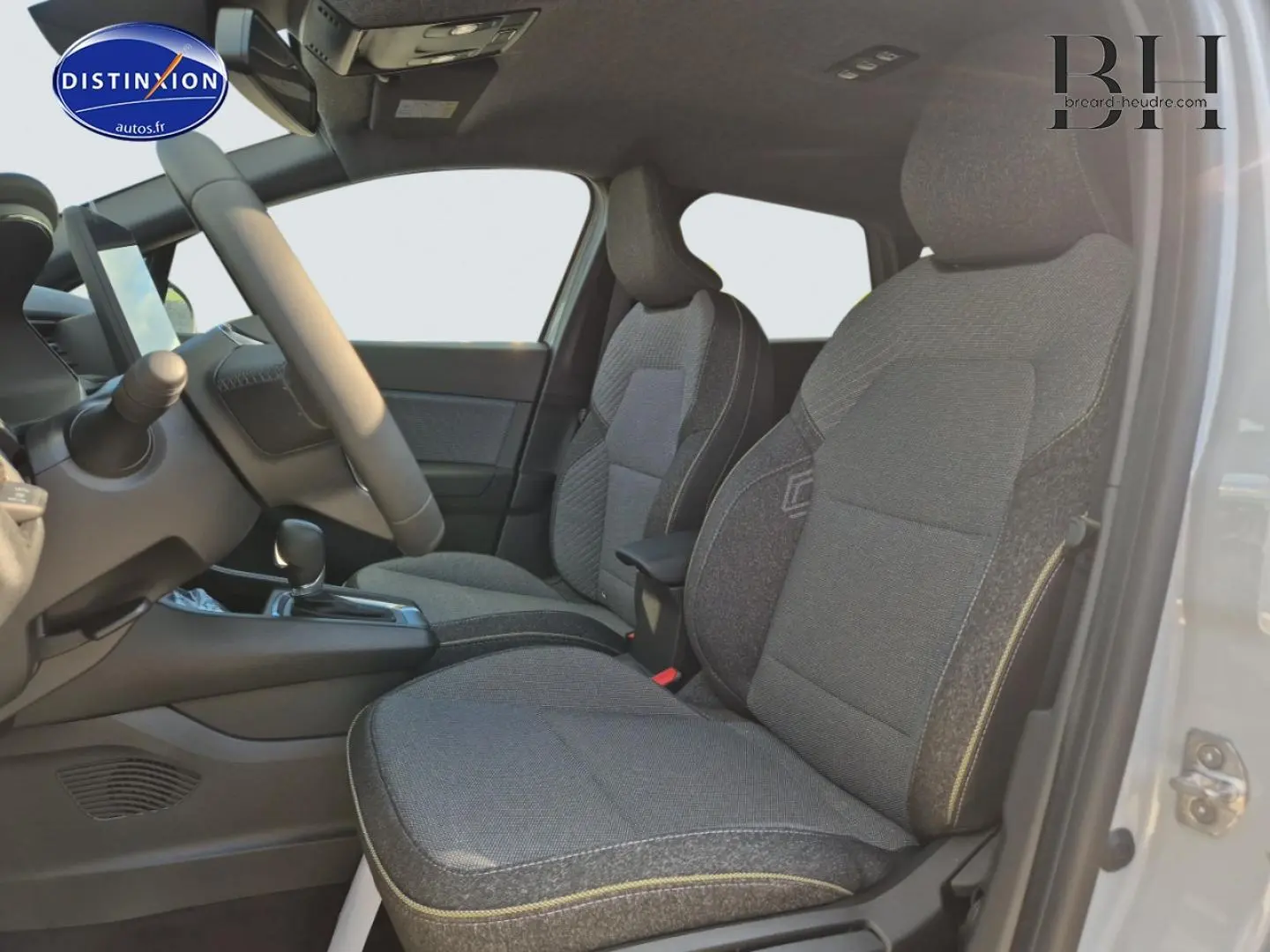 Vue intérieure côté gauche sur les sièges avant gris du Renault Captur 1.6 E-Tech hybride 2025, volant et console visibles.