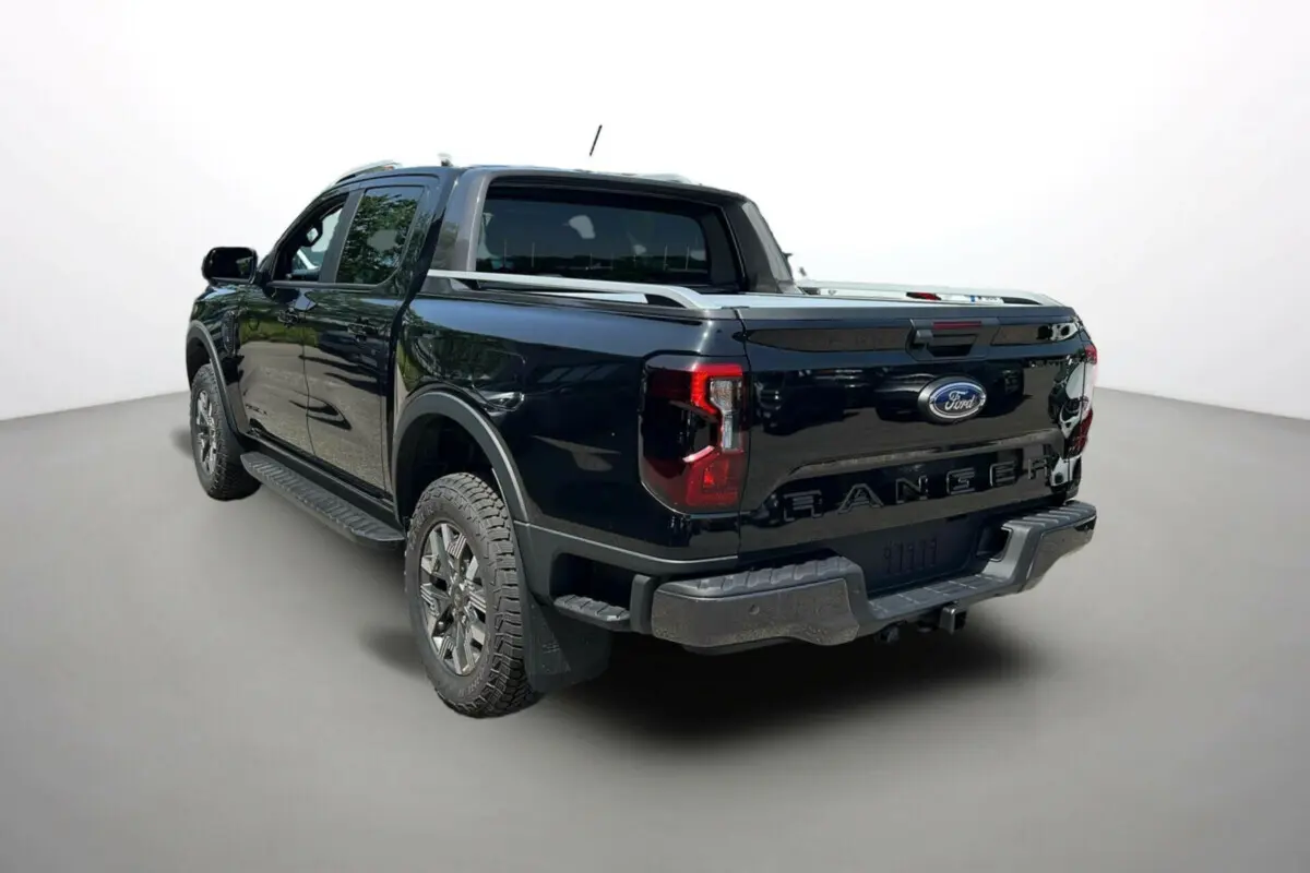 Ford Ranger 2025 noir agate vu en 3/4 arrière droit, avec benne fermée et jantes tout-terrain Wildtrak Plus.