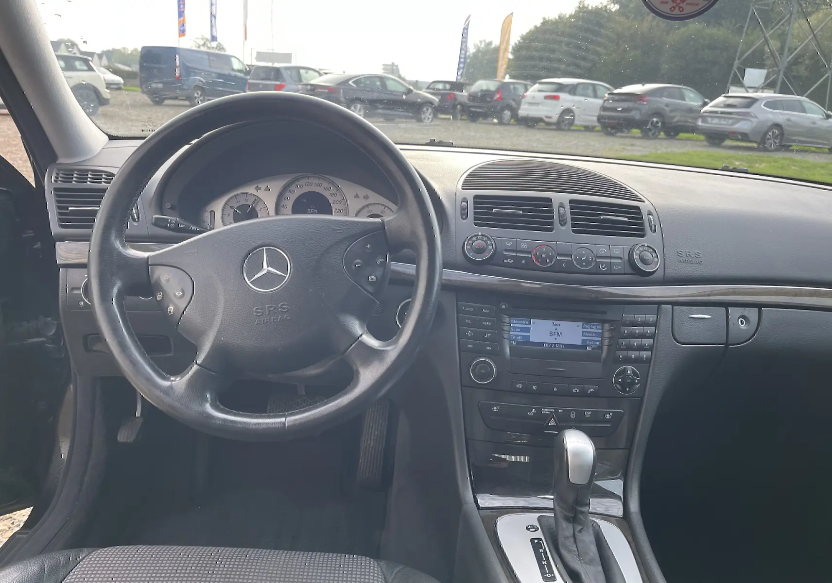Vue intérieure centrée sur le volant et la console centrale d'une Mercedes Classe E noire de 2003 avec boîte automatique.