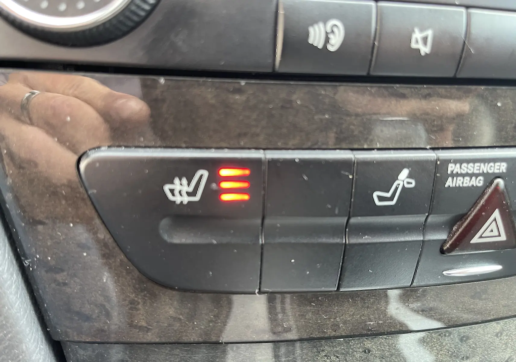 Gros plan sur les commandes de sièges chauffants et airbag passager du tableau de bord d’une Mercedes Classe E noire de 2003.